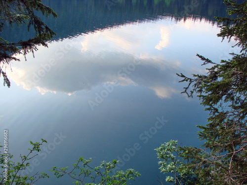 Panorama of a wild mountain lake surrounded by trees of coniferous forest on its banks  on a clean surface of which is reflected by the evening barely cloudy sky.