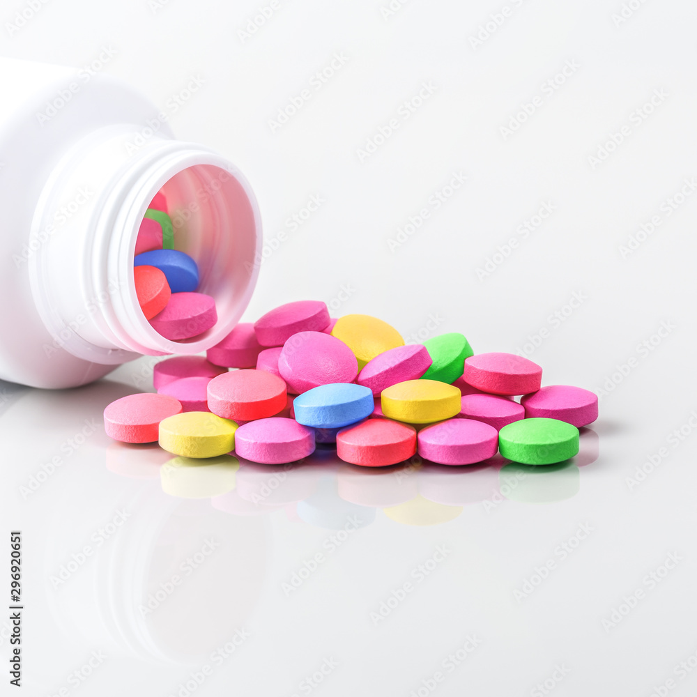 Multicolored pills are scattered from a jar on a white background. Multicolored pills are scattered from a jar on a white background.