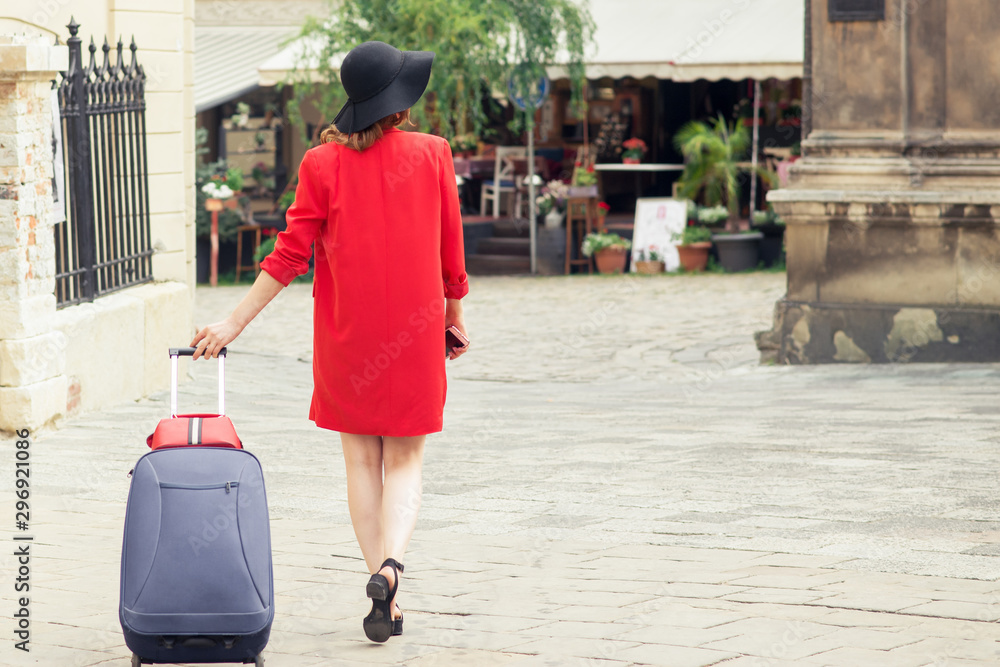 Back view of woman in black hat with suitcase is walking on the city  street. Portrait from behind of traveller girl walks and pulls suitcase.  Stock Photo | Adobe Stock