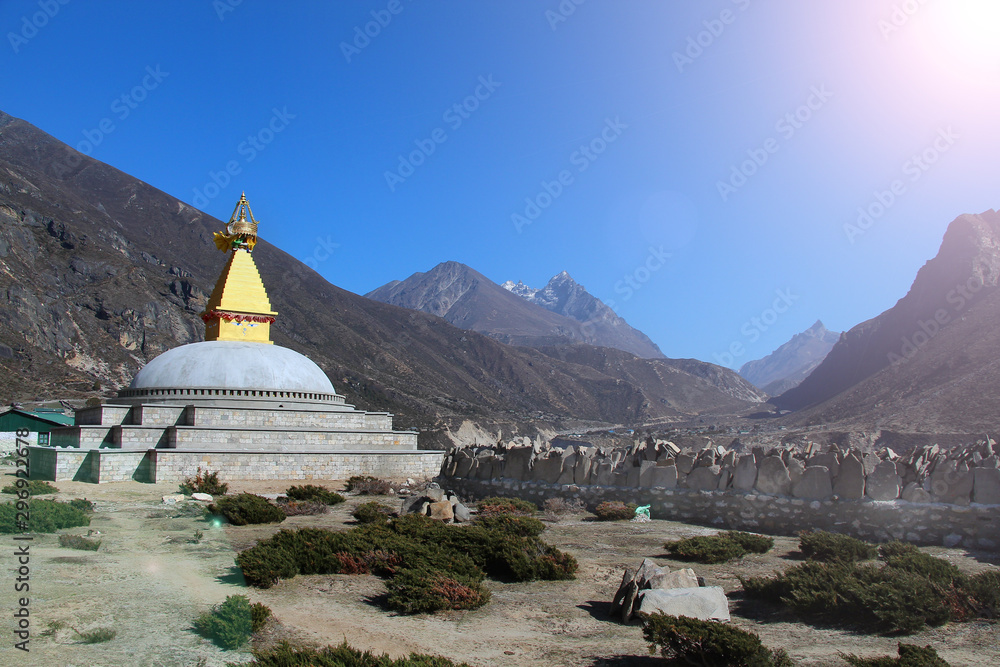 Old typical golden Buddhist stupa (chorten) near mani stones in Thyangmoche village in Himalayas in Nepal with clear sky in the background. Above is a standard drawing of the eyes of Buddha.