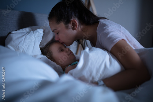 Mother Kissing Her Sleeping Daughter On Bed
