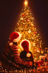 Christmas Family Looking Lighting Xmas Tree, Mother and Child in Red Santa Hats, New Year Night