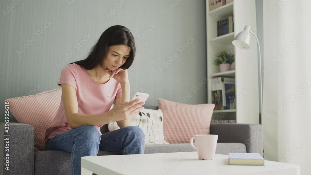 Attractive young woman typing on her smart phone while sitting on the sofa at home. Attractive young woman typing on her smart phone while sitting on the sofa at home.