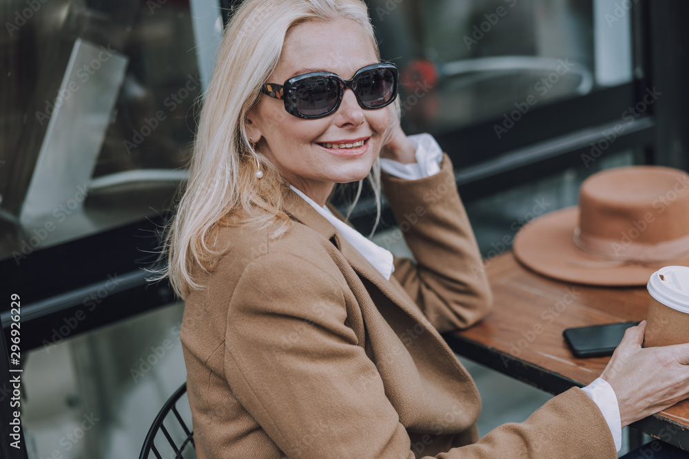 Smiling mature female is wearing sunglasses outdoors