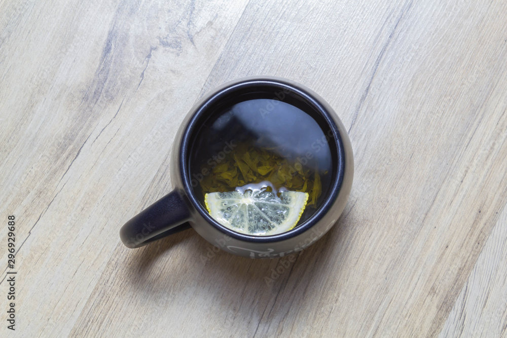 Green tea with lemon in a black cup on a wooden parquet Green tea with lemon in a black cup on a wooden parquet