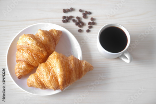 Close up Croissants with coffee. Two french croissants on white plate and cup of espresso coffee on wood table.