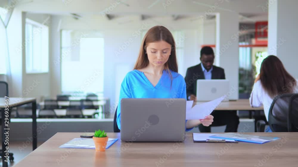 caucasian girl office employee with blond hair working with pc at workplace young businesswoman in casual blue shirt has talking by phone sitting at desk caucasian girl office employee with blond hair working with pc at workplace young businesswoman in casual blue shirt has talking by phone sitting at desk