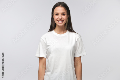 Portrait of smiling young woman in white t-shirt looking at camera, isolated on gray background