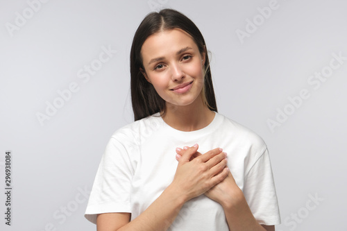 Fotografija Portrait of smiling positive young woman keeps hands on chest, expresses sympathy