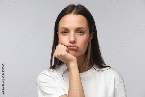 Foto Portrait of bored young woman with head on chin isolated on gray background