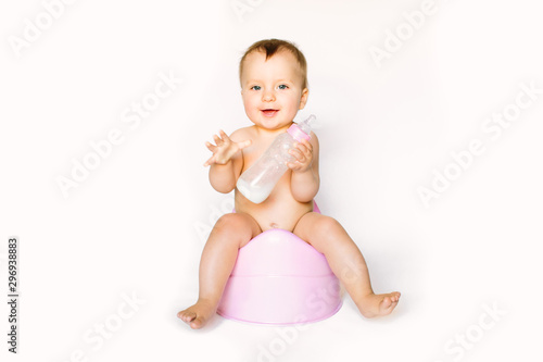 Charming photo of cute baby girl holding a boottle with baby milk and sitting on a pink potty. Isolated on white background