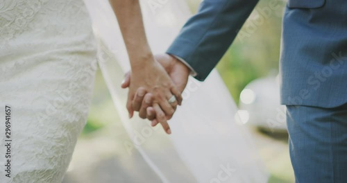 Close up shot of a bride and grooms hands interlocked showing a diamond ring, close up of couple holding hands on their wedding day walking together down the aisle photo