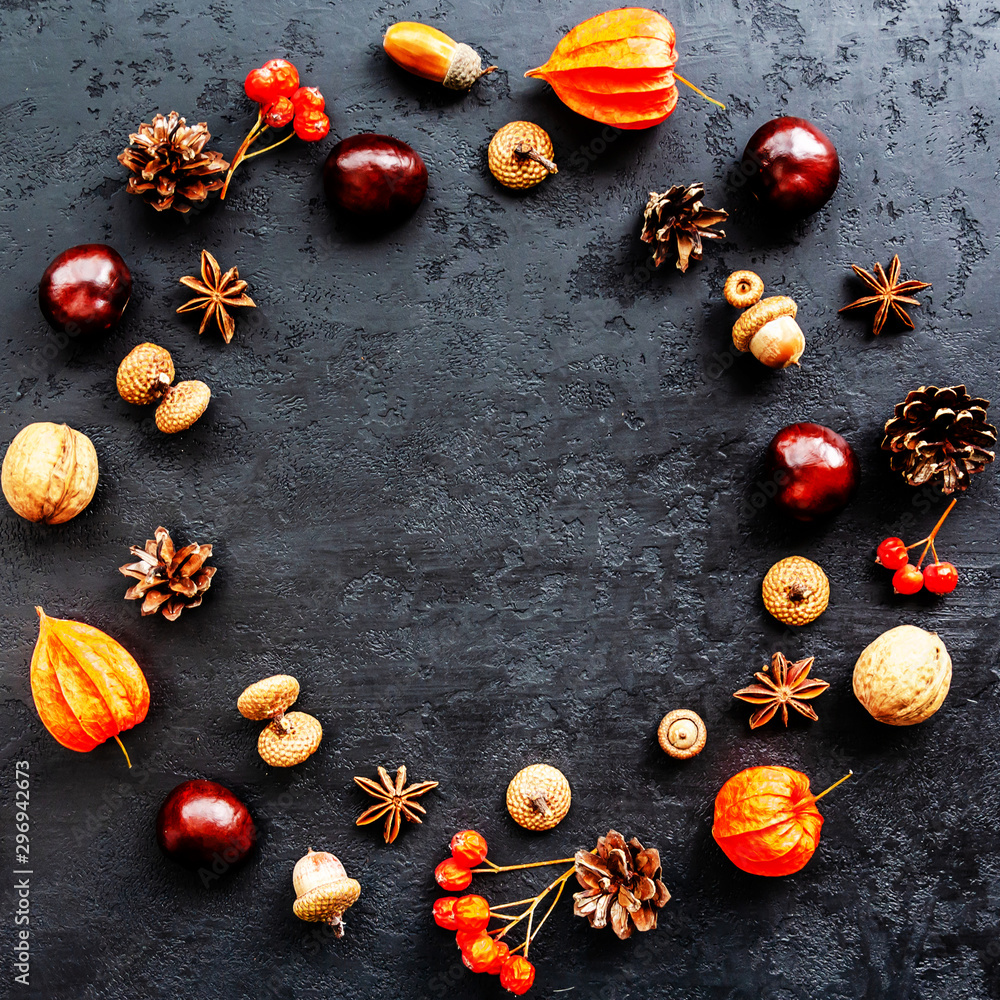 Autumn composition. Wreath made of acorns, chestnuts, pine cones, walnuts, anise stars, physalis, rowan berries on black background. Round frame. Flat lay, top view, copy space