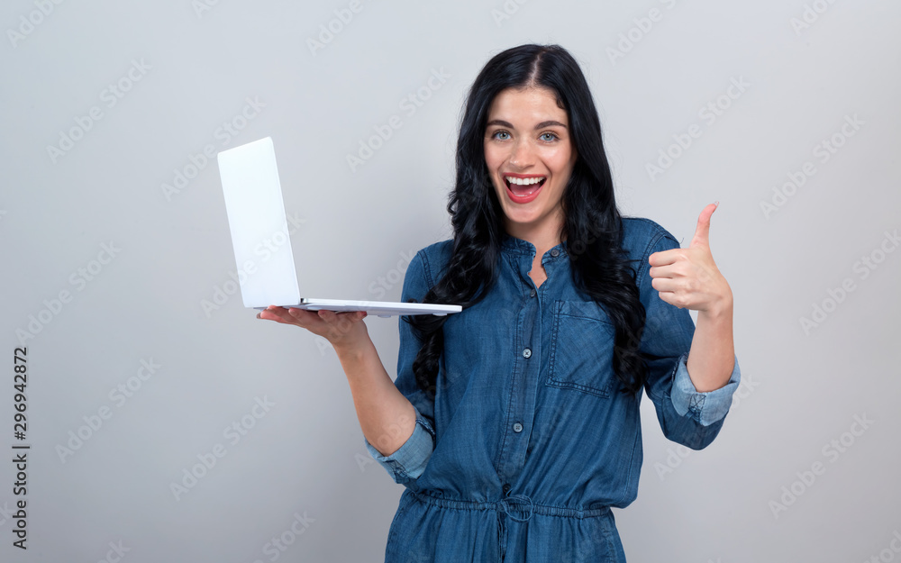 Young woman with a laptop computer giving thumb up on a gray background Young woman with a laptop computer giving thumb up on a gray background