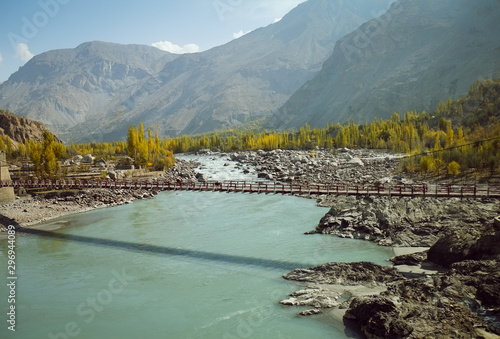 Indus river flowing through mountainous area in Ghanche district with a view of colorful trees in autumn season against Karakoram mountain range. Gilgit Baltistan, Pakistan. photo