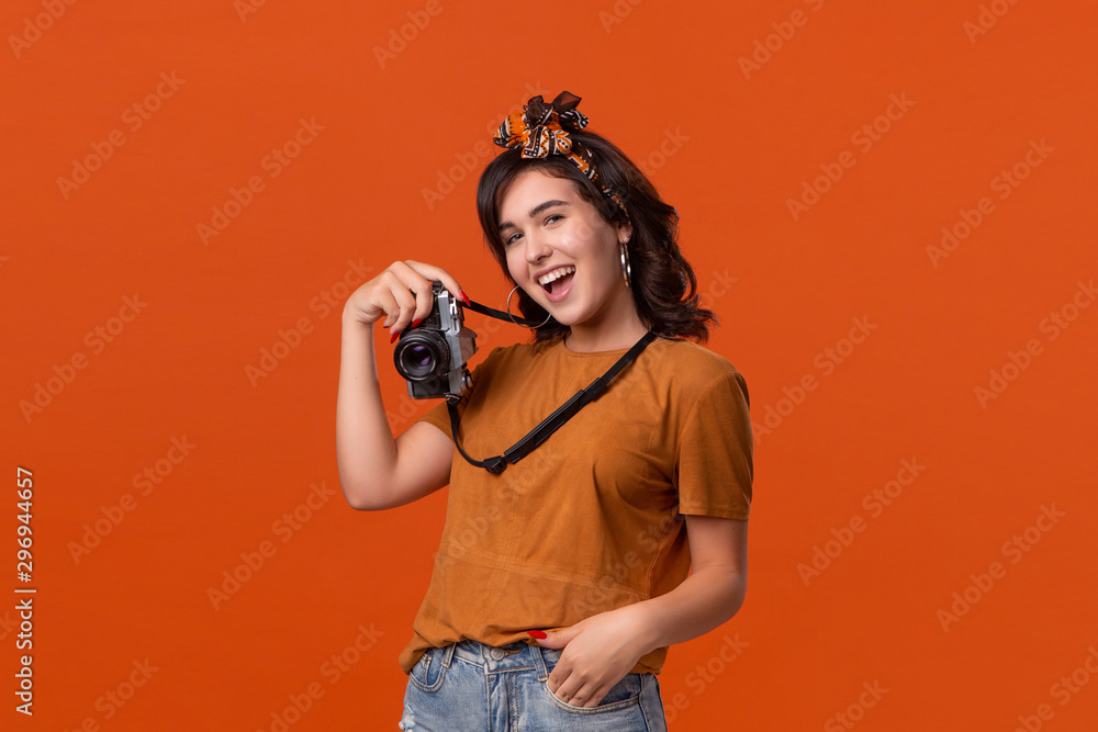 Obraz premium Pretty brunette woman making photo with a retro film camera standing isolated on an orange background.