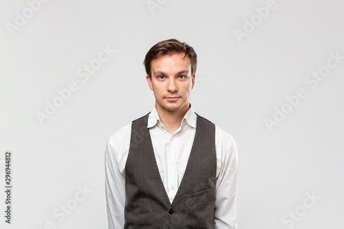 Confindent handsome man in a white shirt and grey vest looking at the camera standing isolated over grey background.