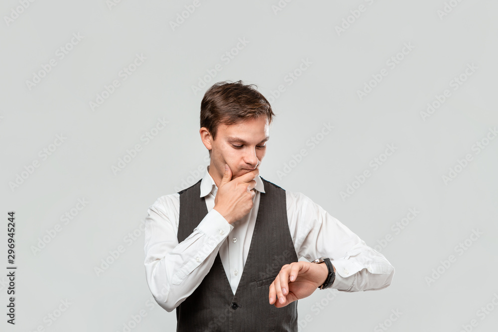 Young businessman in a white shirt and grey vest checking time on his wrist watch. Concept of punctuality Young businessman in a white shirt and grey vest checking time on his wrist watch. Concept of punctuality