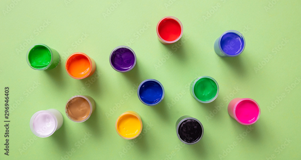 Colorful finger paints set on green color background, top view