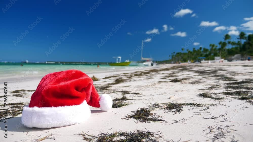 Christmas Santa Claus hat on tropical sandy shore with calm waves. Winter holidays. New Year celebration on caribbean island