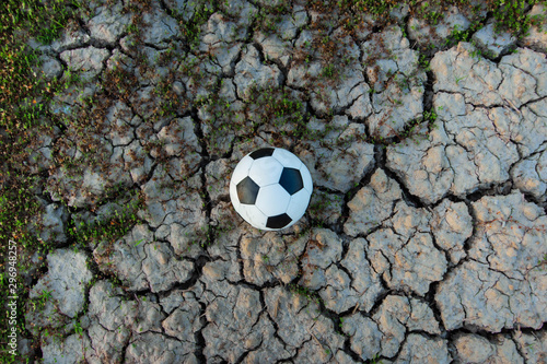 Fototapeta Naklejka Na Ścianę i Meble -  The football ball in a field that is dry and cracked in the evening sun