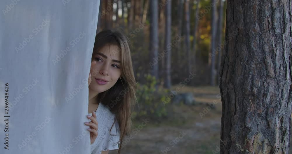 Young beautiful Caucasian woman peeking out of white clothing and smiling. Attractive positive girl enjoying calm summer day in the forest. Young beautiful Caucasian woman peeking out of white clothing and smiling. Attractive positive girl enjoying calm summer day in the forest.