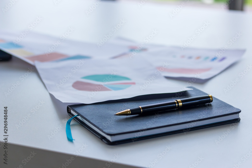 A pen on a businessman's book with a graph paper on the desk A pen on a businessman's book with a graph paper on the desk