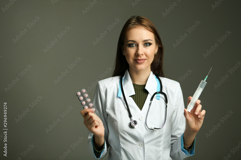 beautiful young woman doctor holds a syringe in one hand and pills in the other hand on a gray background. conceptual photo about choosing between an injection and pills beautiful young woman doctor holds a syringe in one hand and pills in the other hand on a gray background. conceptual photo about choosing between an injection and pills