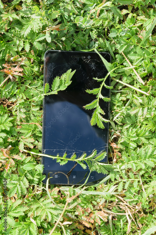 A lost smartphone is overgrown with grass. The touch screen is broken. A lost smartphone is overgrown with grass. The touch screen is broken.