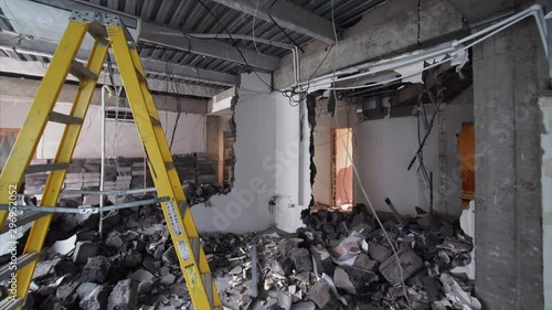 Sliding view of demolition work in apartment. Ladder is in the middle of the room full of broken bricks and blocks from broken walls photo