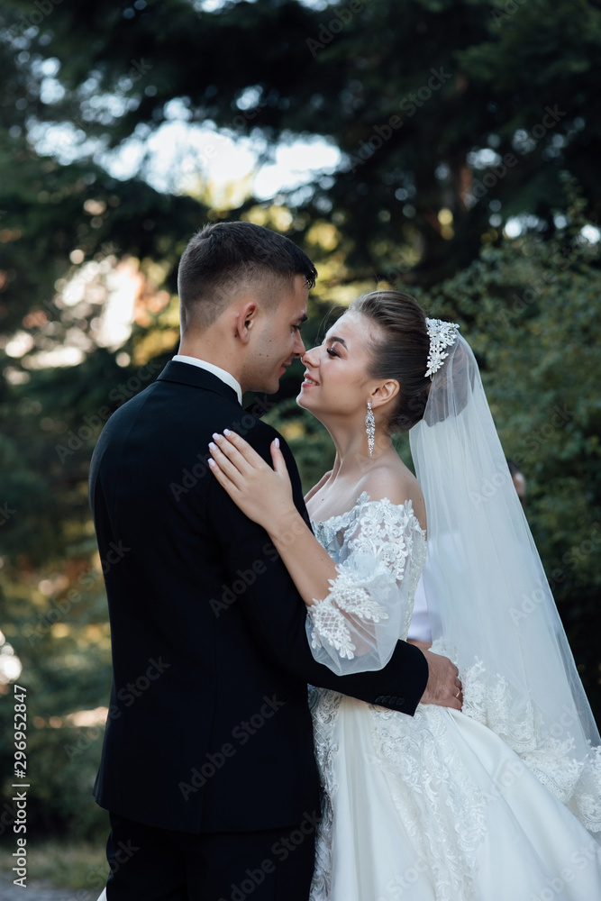 Stylish bride and groom gently kissing. Beautiful bride with modern bouquet embracing with stylish groom in summer park. Sensual romantic moment. Wedding. Stylish and beautiful. Stylish bride and groom gently kissing. Beautiful bride with modern bouquet embracing with stylish groom in summer park. Sensual romantic moment. Wedding. Stylish and beautiful.