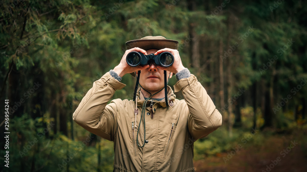 A man in a hat and uniform green and beige holds binoculars and looks into the distance, Ranger watching the territory, the protection of the reserve A man in a hat and uniform green and beige holds binoculars and looks into the distance, Ranger watching the territory, the protection of the reserve