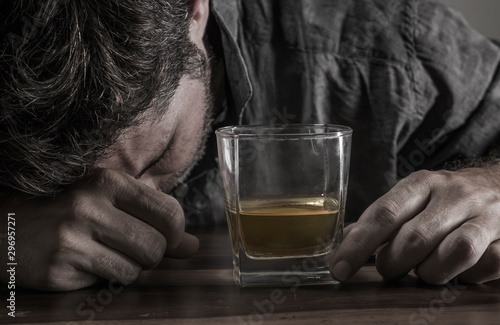 depressed and thoughtful alcoholic man on his 40s in front of whiskey glass wasted and stressed holding on temptation to drink in alcohol addiction and alcoholism problem