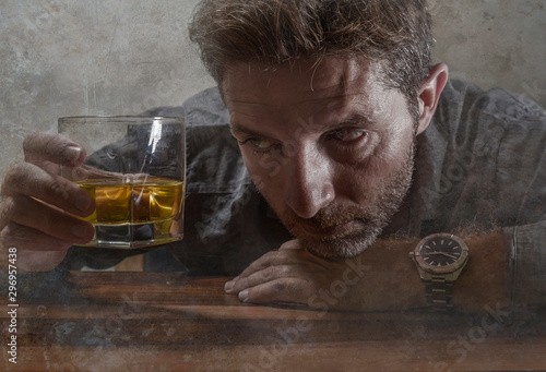 alcoholic depressed and wasted addict man sitting in front of whiskey glass trying holding on drinking in dramatic expression suffering alcoholism and alcohol addiction