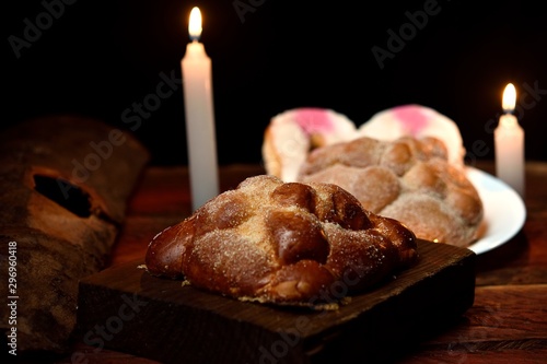 Mexican tradition. Dead bread made with butter and egg, placed on a square wooden base in turn on wooden logs. Background with candles and diffused or unfocused lights photo