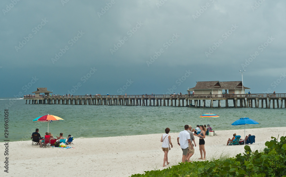 Front view, long distance of people on a tropical, sandy, beach standing and siting watching storm clouds move toward shore 