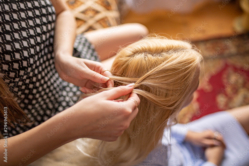 Fototapeta premium woman braids braids to a young girl. Female hands weave braids