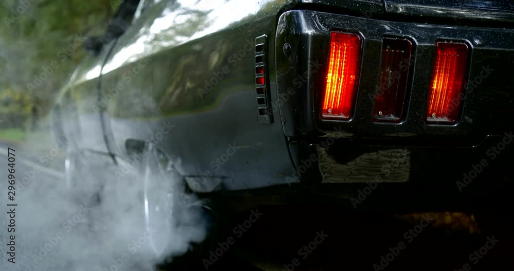 Close-up of the back of a classic car, smoke coming from under the rear