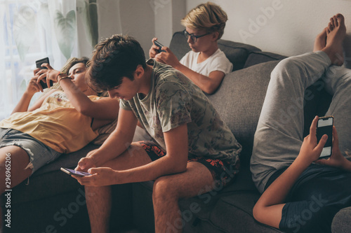 Group of teenager using smartphone sitting on a sofa at home. Young boys and a girl sharing photo and video watching social story online. Friends enjoying new trend technology. Youth and tech concept photo