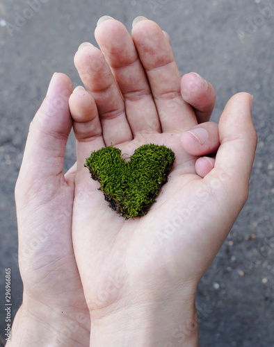 The palm of a man holds the palm of a woman in which lies a small moss in the form of a heart of green color