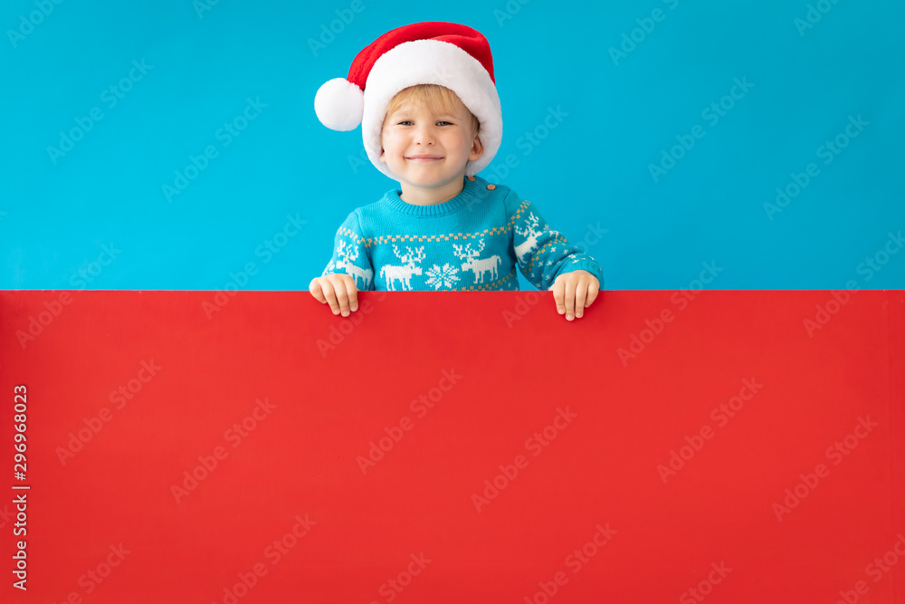 Happy child holding red Christmas banner blank against blue background Happy child holding red Christmas banner blank against blue background