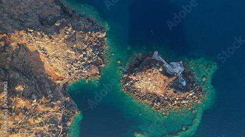 Aerial drone photo of picturesque volcanic with black rock islet and chapel of Agios Nikolaos in bay of Amoudi below iconic village of Oia, Santorini island, Cyclades, Greece