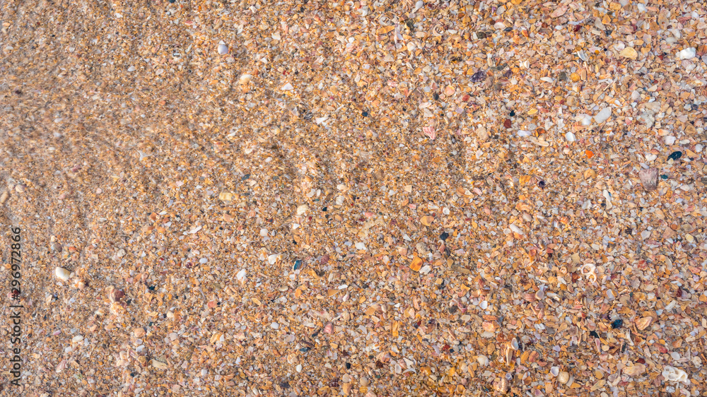 Beach sand texture. Broken seashells background. Colorful sand surface of a beach with clear sea water. Waves. Beach sand texture. Broken seashells background. Colorful sand surface of a beach with clear sea water. Waves.