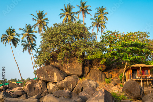 Amazing view of tropical beach. Green trees, palms and touristic cabin on blue sky background. 