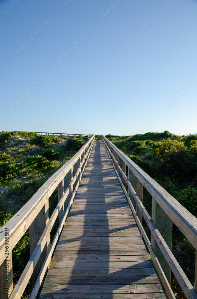 Wooden boardwalk crossing the sand dunes heading to the ocean. Oak Island NC beach in the background.