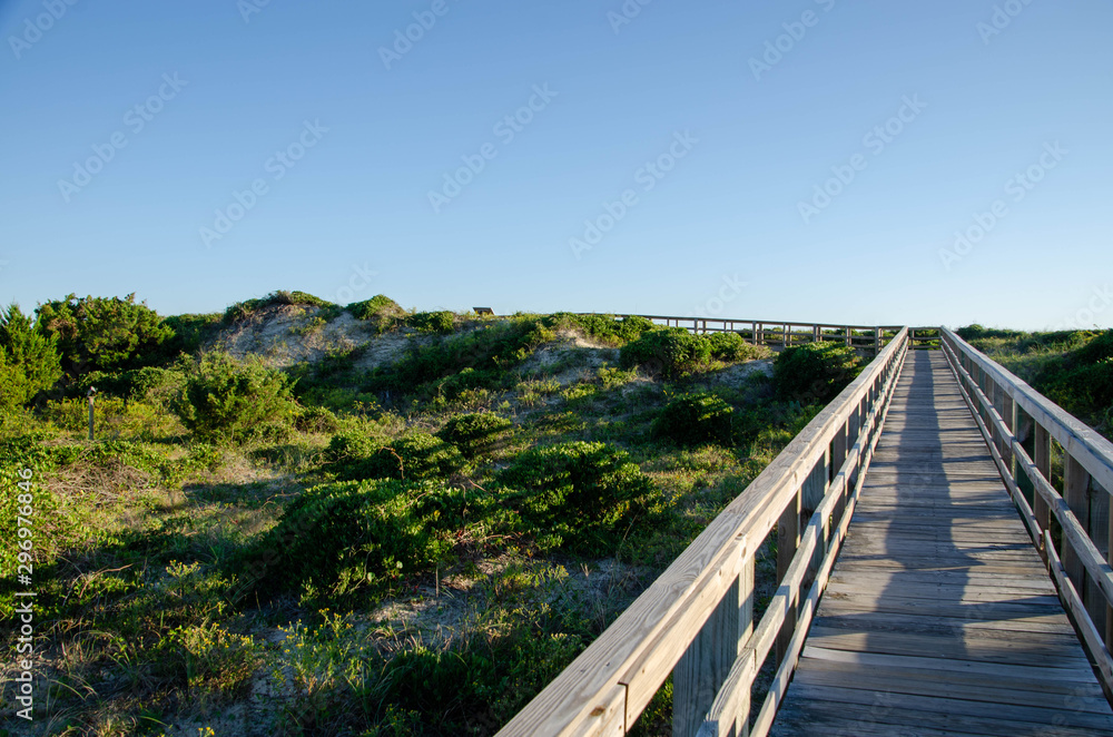 Wooden boardwalk crossing the sand dunes heading to the ocean. Oak Island NC beach in the background.