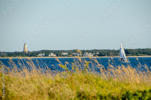 Sailboat sailing out of the Cape Fear river into the ocean at Oak Island. Baldhead Island in the background.