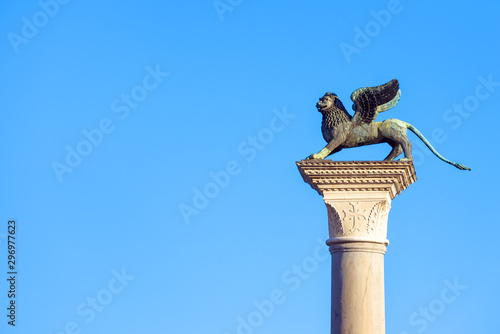 Lion statue at Piazza San Marco (St Mark`s Square) on blue sky background, Venice, Italy. This place is a tourist attraction of Venice city. Winged lion is an ancient and famous symbol of Venice.  photo