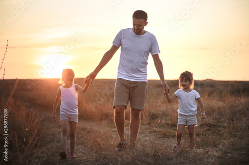 Dad and his daughters in the field at sunset .