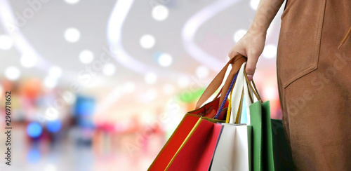 Photos Part of female hand holding shopping paper bags with blurred background of shopp